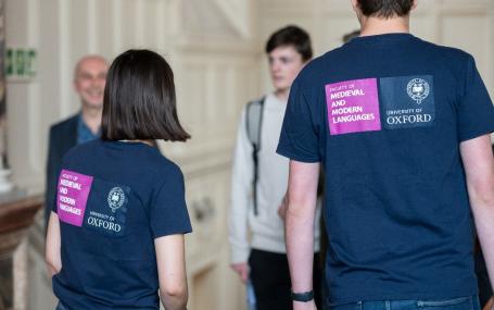The backs of two student ambassadors wearing Faculty t-shirts at an event