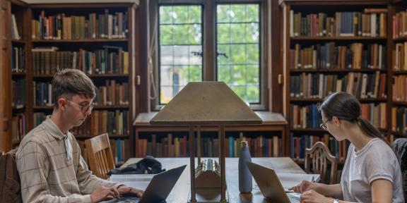 Two students sat on laptops in a library