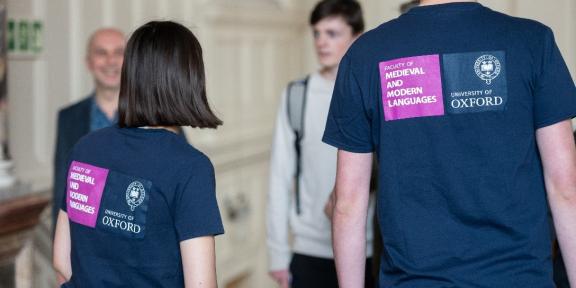 The backs of two student ambassadors wearing Faculty t-shirts at an event