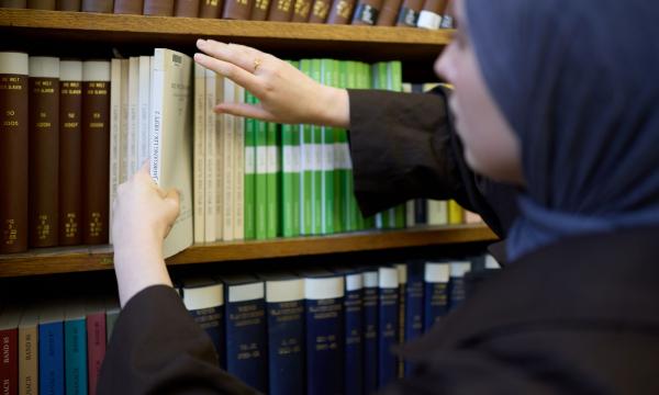 A close up image of a student selecting a book from a shelf of books in the library