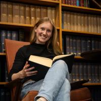 Rebecca sits on a chair and holds a book.