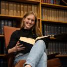Rebecca sits on a chair and holds a book.