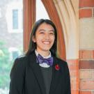 a person wearing a bowtie near a brick pillar with a Gothic window in the background